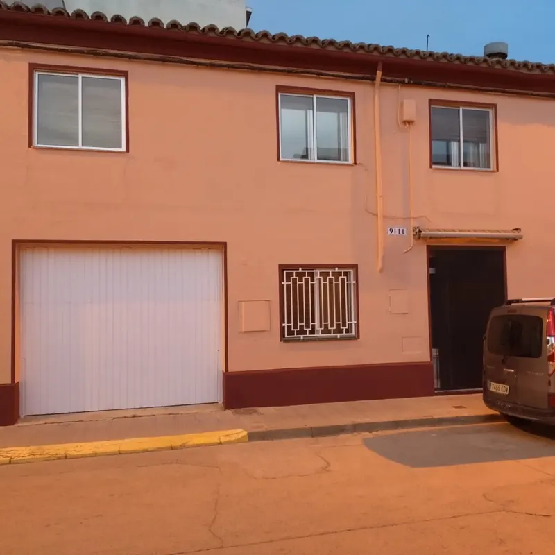 Fachada de la misma vivienda después de pintar, en tono salmón con zócalo granate