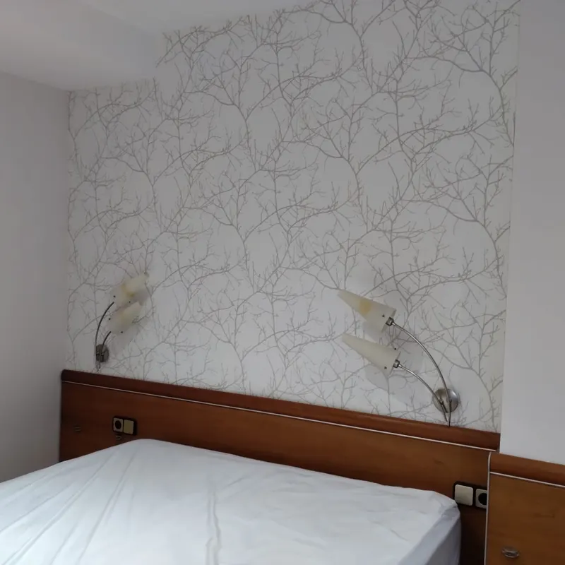 Dormitorio después del trabajo: cabecera con papel pintado claro de ramas y paredes en blanco