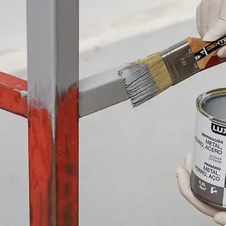 Imprimación gris aplicada con brocha sobre una estructura metálica pintada de rojo